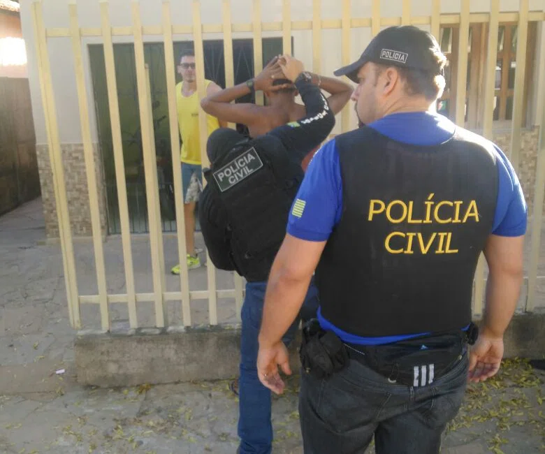 Policiais civis realizando vistoria em um preso.