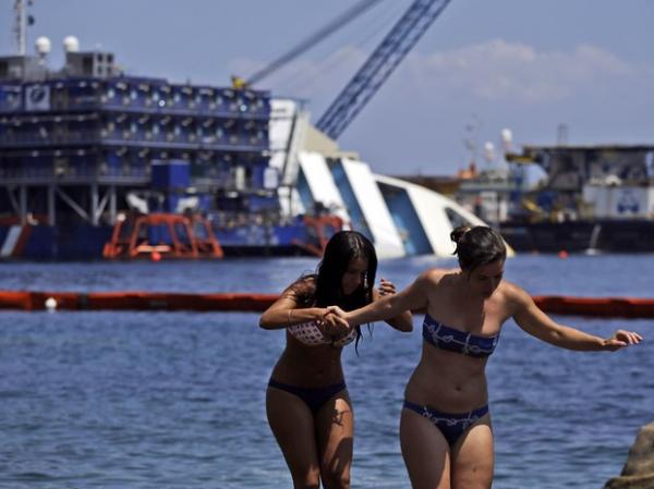 Banhistas caminham sobre pedras próximo ao local onde o Costa Concordia encalhou, na ilha toscana de Isola del Giglio(Imagem:Reprodução)