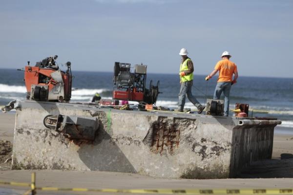 Homens começam a trabalhar na retirada de doca na praia de Agate, ao sudoeste da cidade de Portland (Imagem:Randy L. Rasmussen/AP)